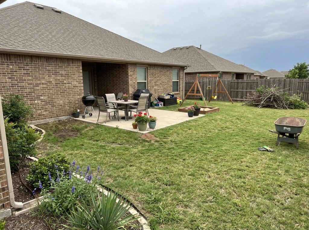 Clean Texas front yard with trimmed shrubs, fresh mulch beds, greener lawn, and a tidy patio with pavers.