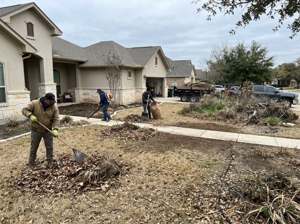 Leaf piles and debris being cleared from garden beds, patio, and walkway in a San Antonio front yard.
