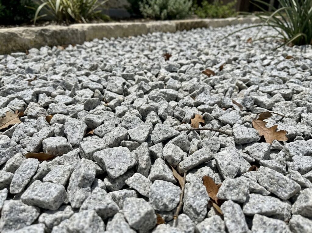 Granite Chips ground cover, close-up of mixed gray and tan crushed stone spread evenly across a landscape bed.