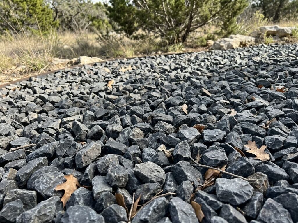 Large Shadow Stone ground cover with dark gray, angular rocks spread in a neat layer for landscaping.